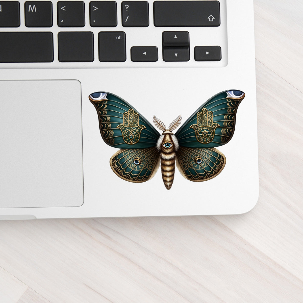 Hamsa Hand Moth UV DTF sticker applied to a silver laptop beside the keyboard