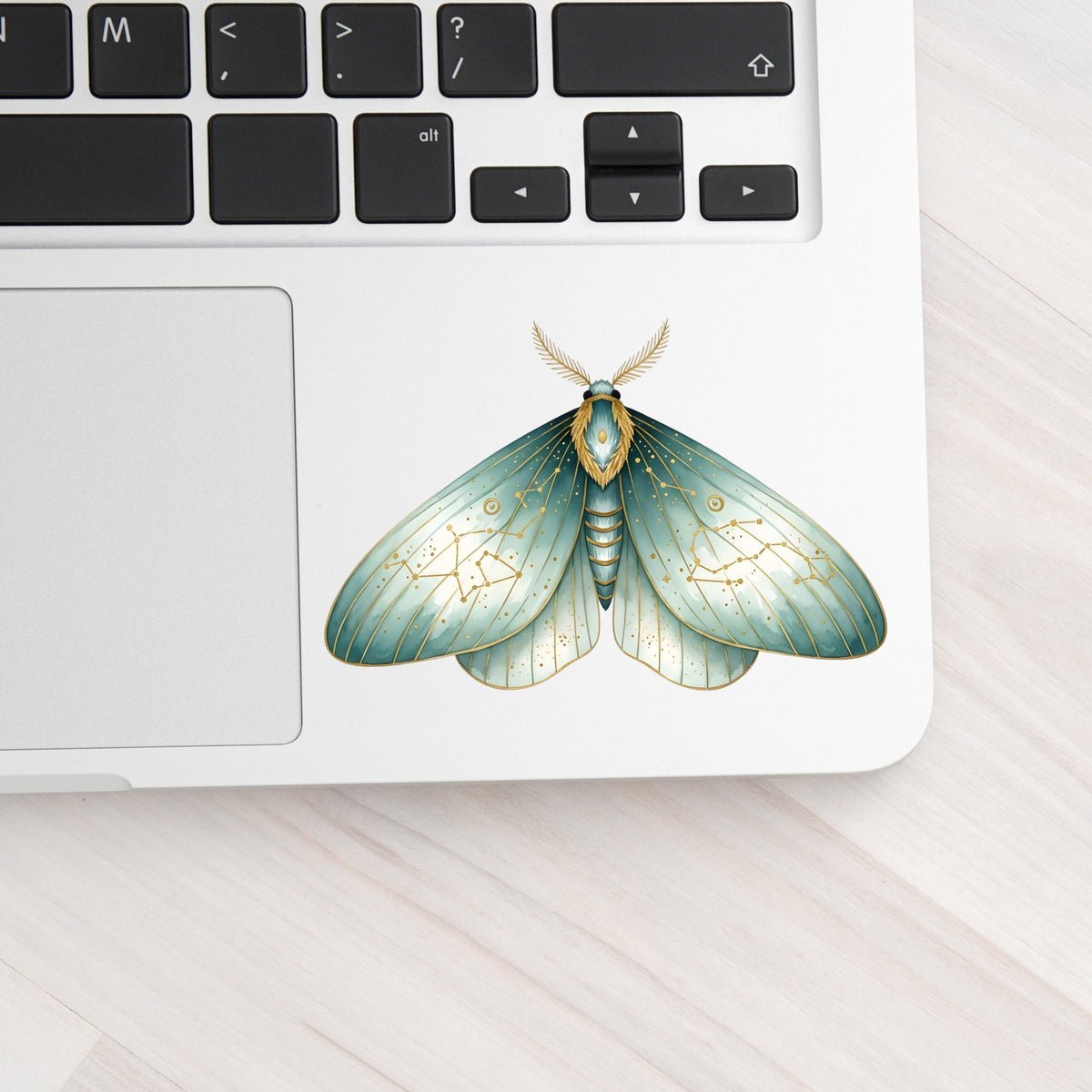 Mint Watercolor Moth UV DTF sticker applied to a silver laptop beside the keyboard