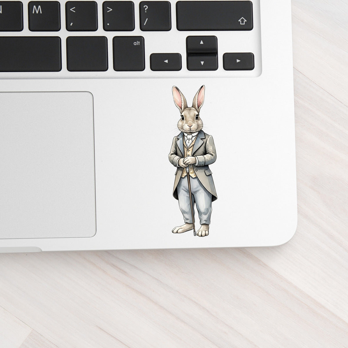 Gray Bunny Victorian Suit Cane UV DTF sticker applied to a silver laptop beside the keyboard