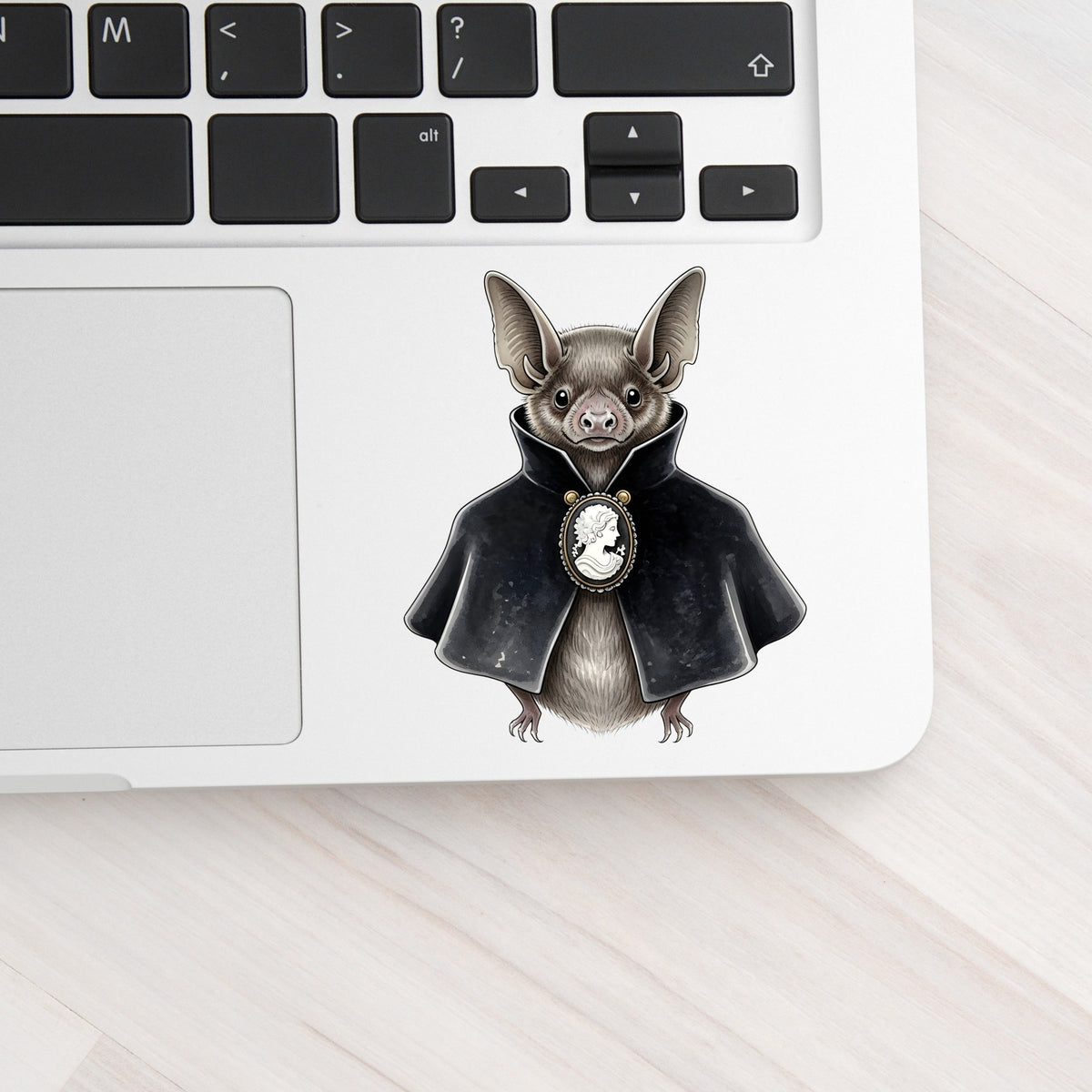 Bat In Black Cape Cameo UV DTF sticker applied to a silver laptop beside the keyboard