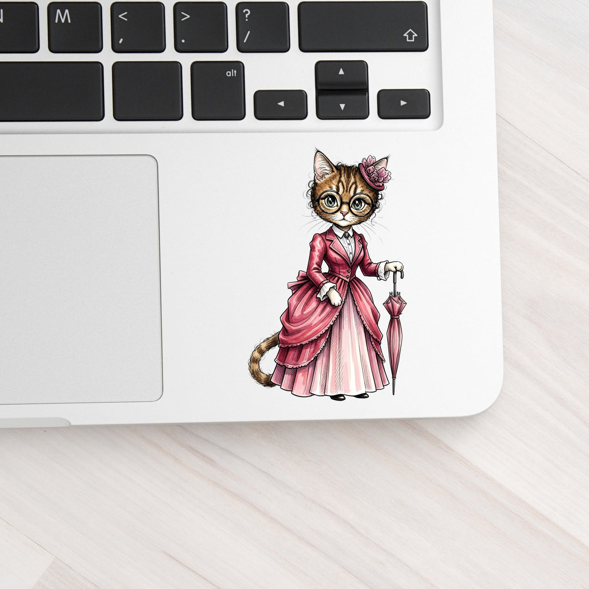 Tabby Cat Pink Victorian Dress UV DTF sticker applied to a silver laptop beside the keyboard
