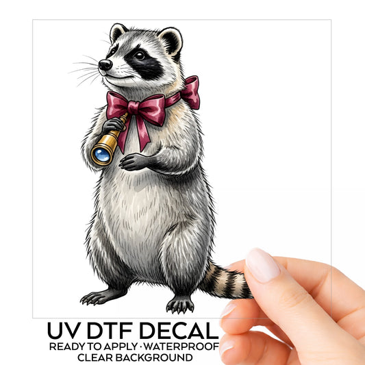 Raccoon With Spyglass Red Bow UV DTF sticker on its backing card, held in hand