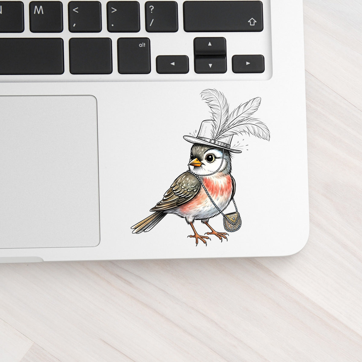 Fancy Bird Feather Hat Purse UV DTF sticker applied to a silver laptop beside the keyboard
