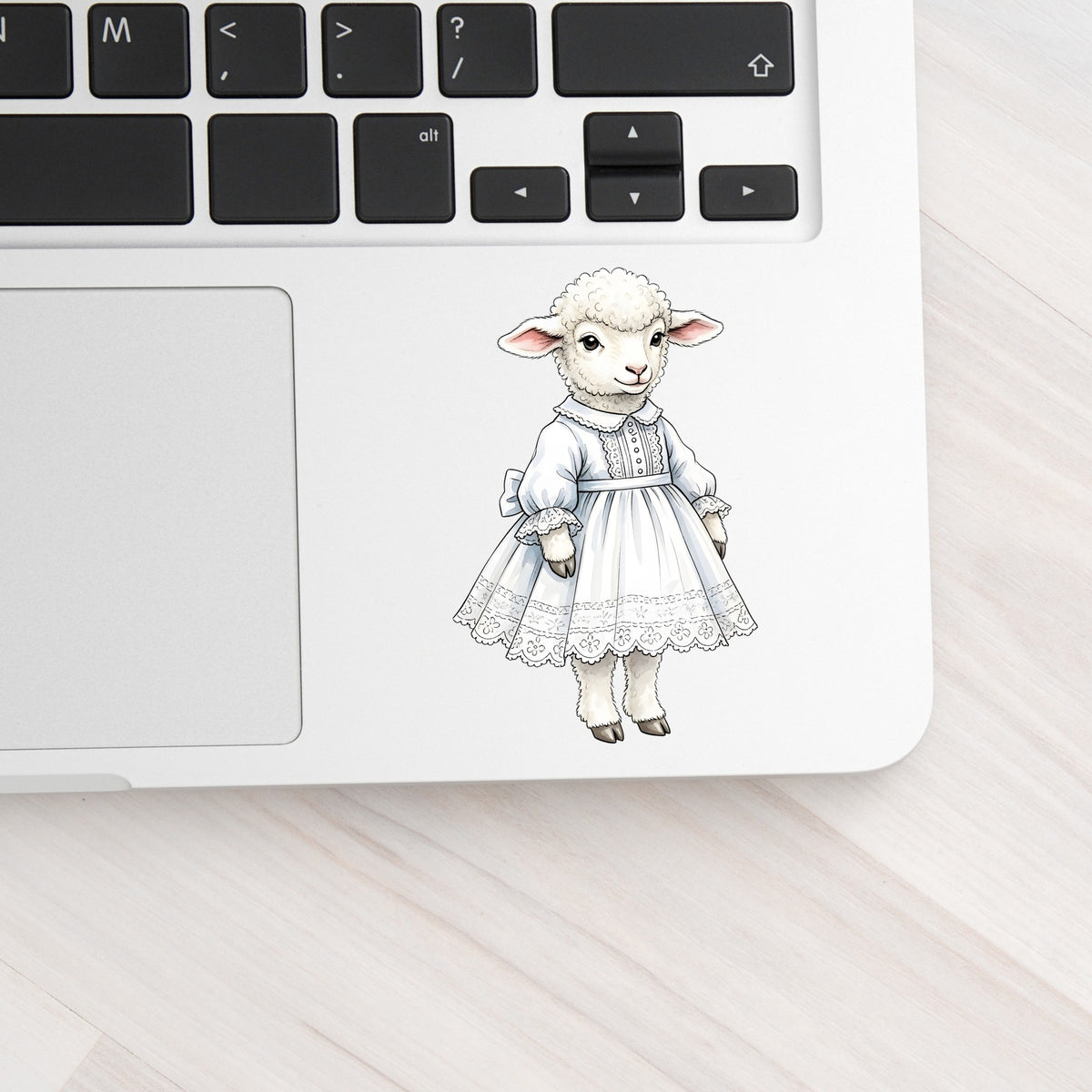 Lamb In White Lace Dress UV DTF sticker applied to a silver laptop beside the keyboard