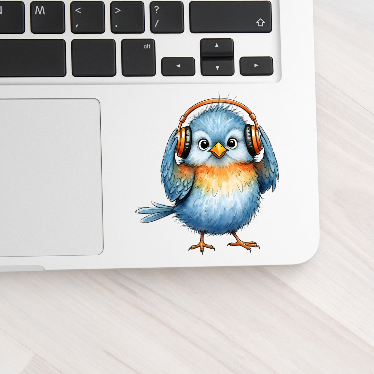 Blue Bird With Headphones UV DTF sticker applied to a silver laptop beside the keyboard