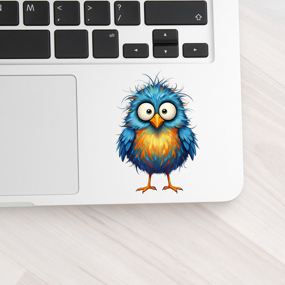 Chaotic Fuzzy Blue Bird UV DTF sticker applied to a silver laptop beside the keyboard