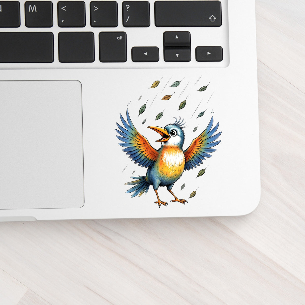 Happy Bird Wings Spread Falling Leaves UV DTF sticker applied to a silver laptop beside the keyboard