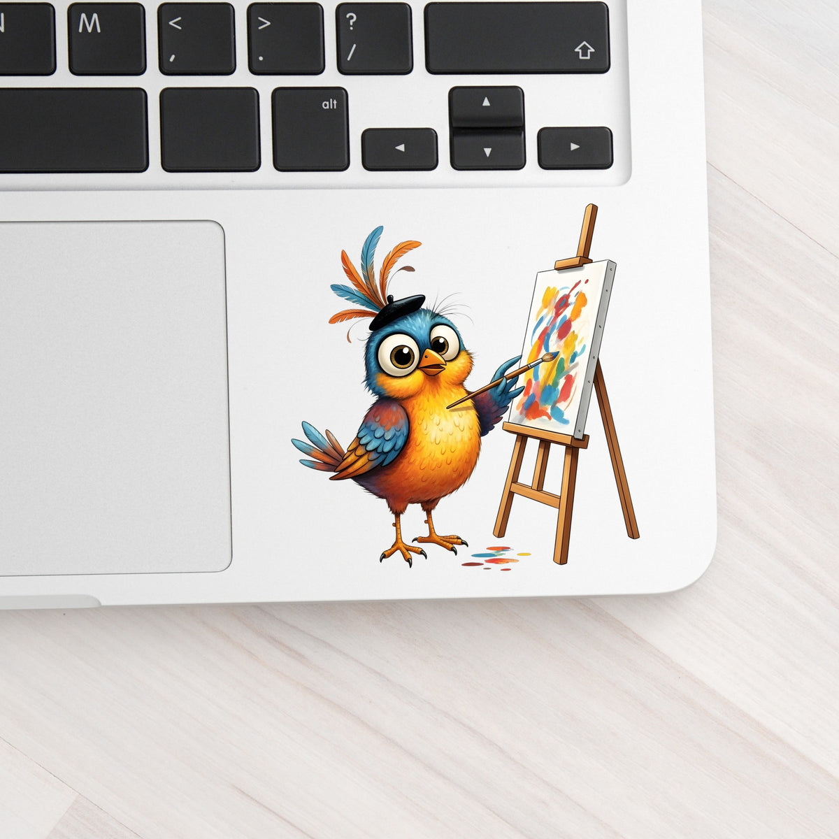 Artist Bird Painting Easel Beret UV DTF sticker applied to a silver laptop beside the keyboard