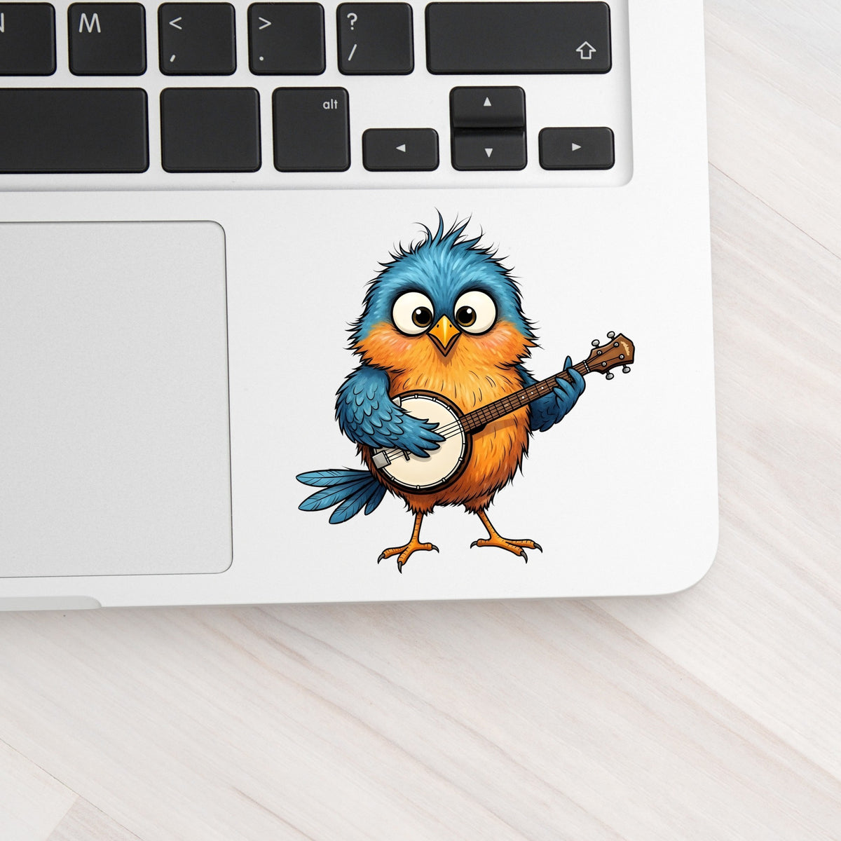 Bird Playing Banjo UV DTF sticker applied to a silver laptop beside the keyboard