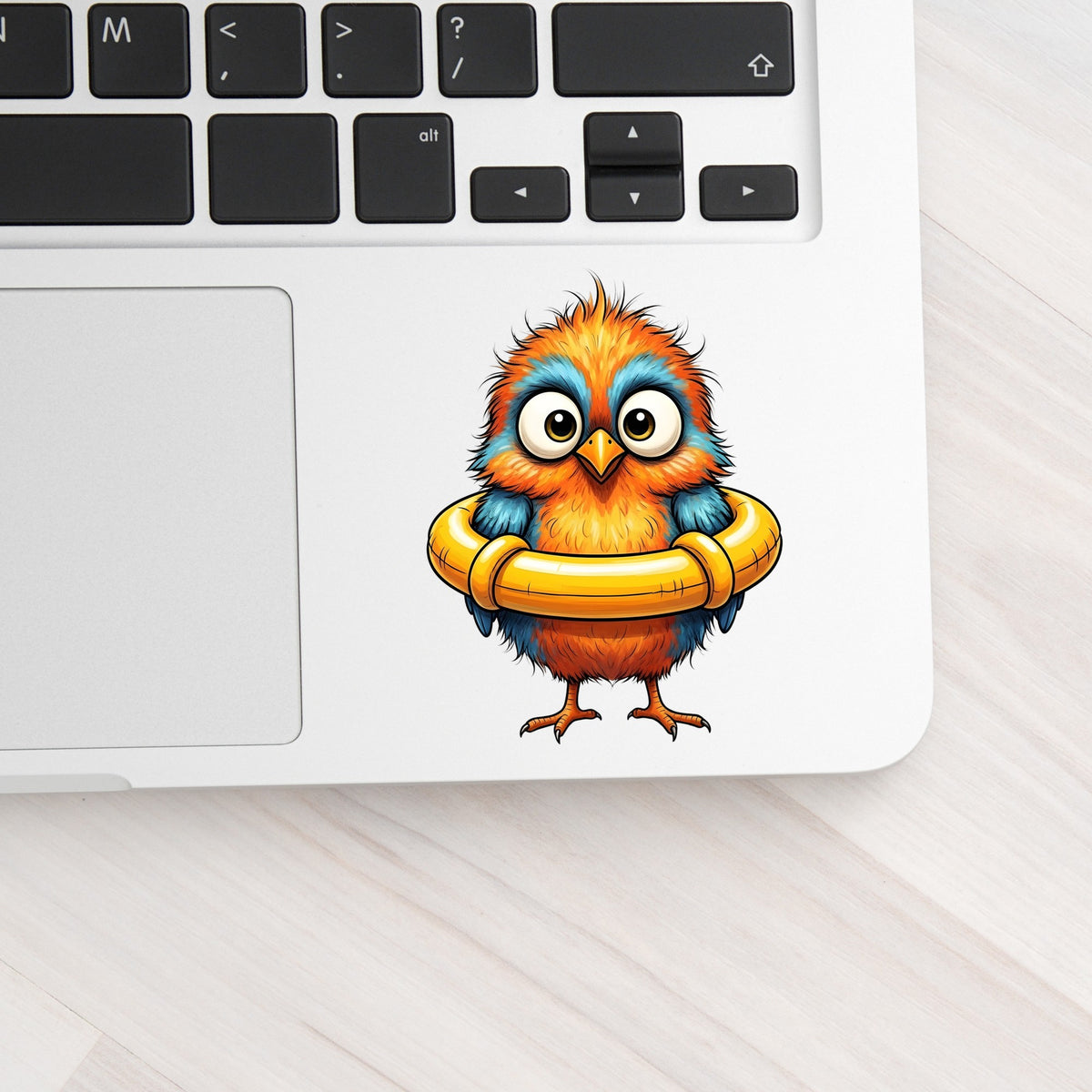 Orange Bird In Swim Ring UV DTF sticker applied to a silver laptop beside the keyboard