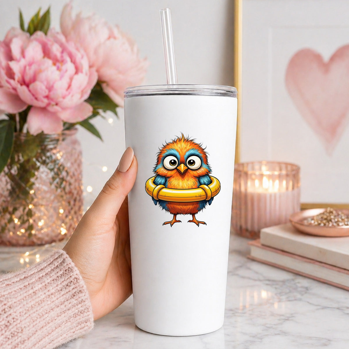 Orange Bird In Swim Ring UV DTF sticker applied to a white straw tumbler beside pink peonies