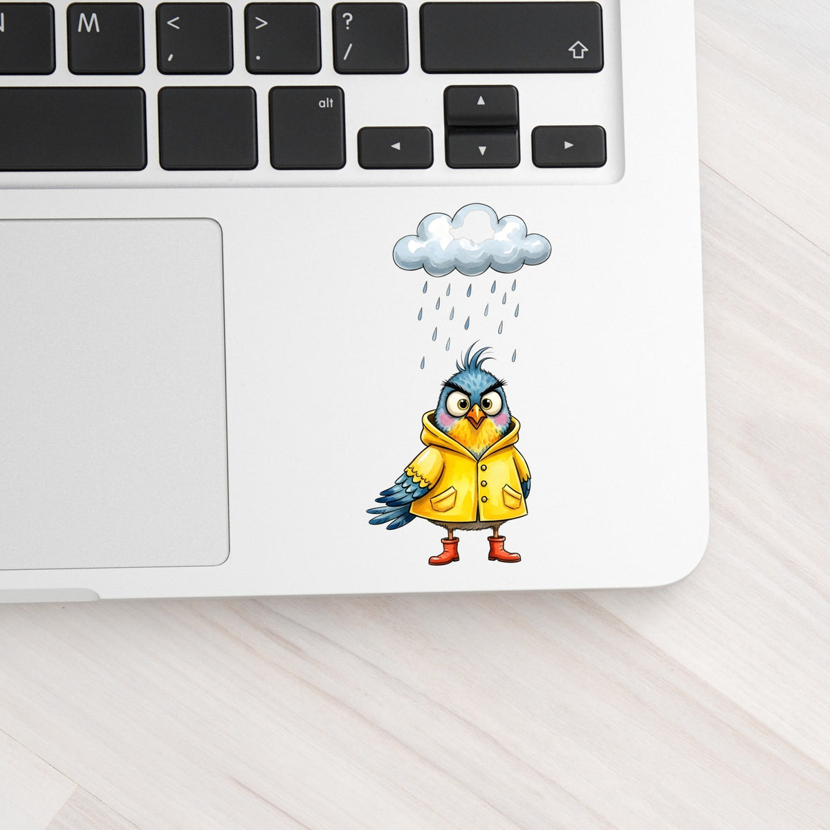 Rain Cloud Bird Yellow Raincoat UV DTF sticker applied to a silver laptop beside the keyboard