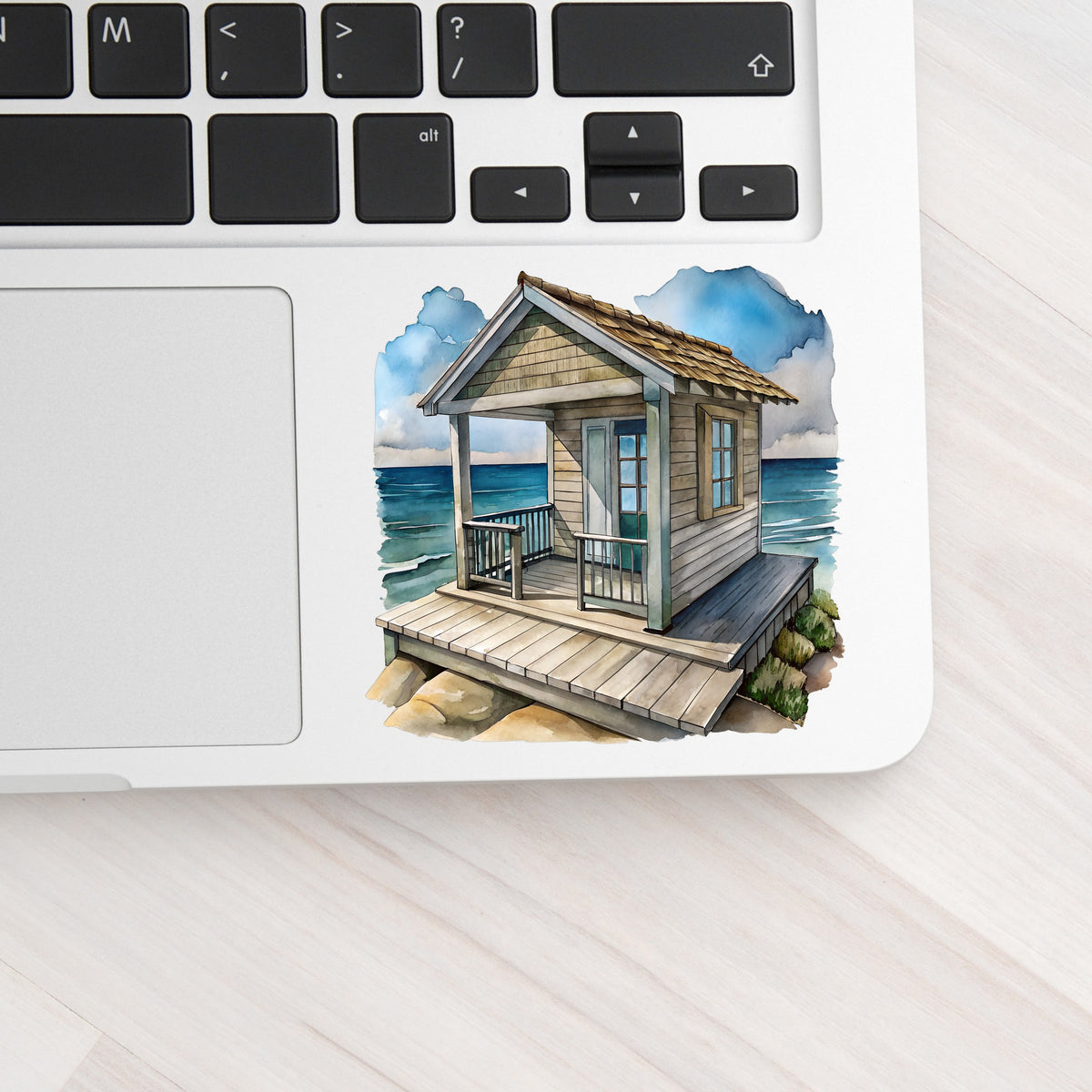 Beach Cottage Porch Ocean View UV DTF sticker applied to a silver laptop beside the keyboard