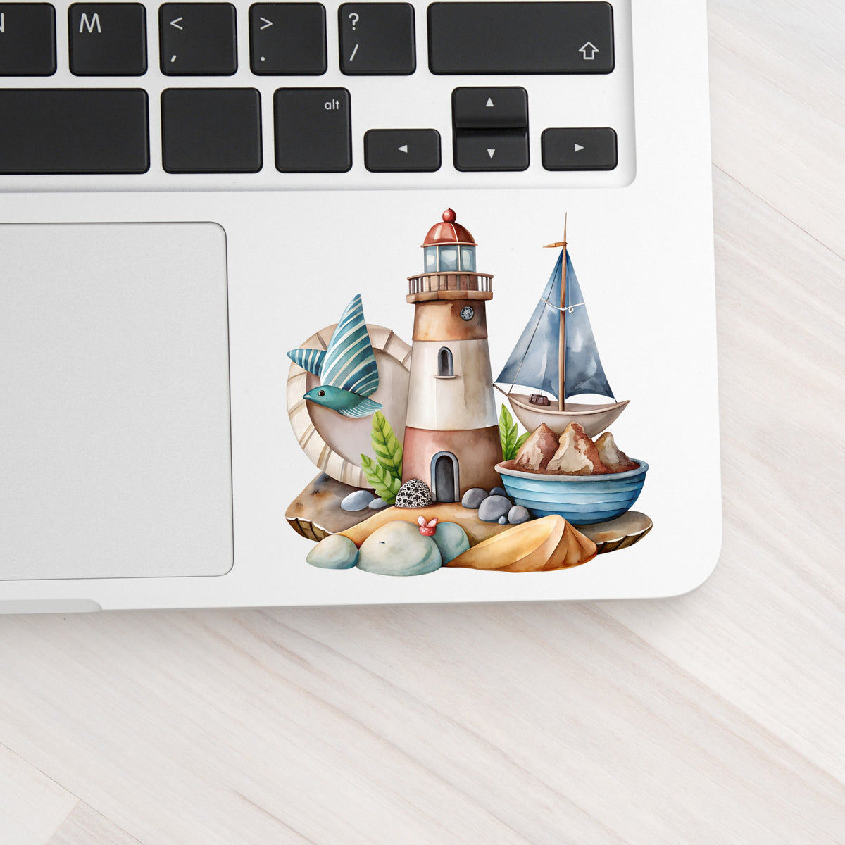 Lighthouse Sailboat Seaside Scene UV DTF sticker applied to a silver laptop beside the keyboard