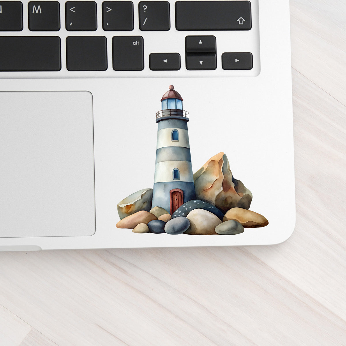Lighthouse On Rocky Shore UV DTF sticker applied to a silver laptop beside the keyboard