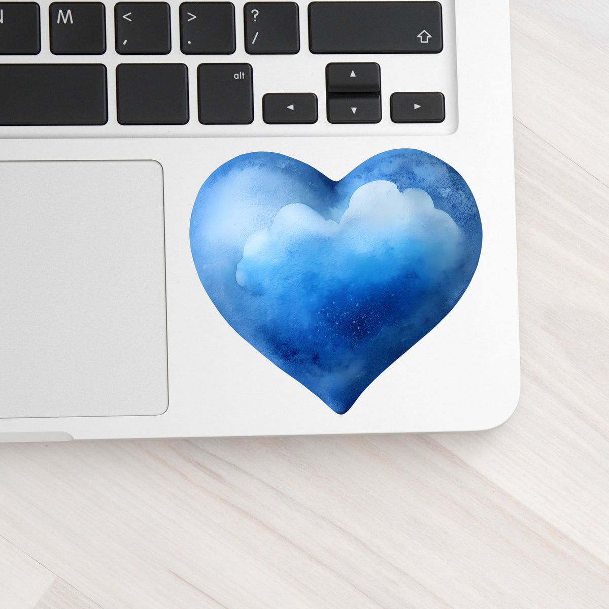 Blue Watercolor Heart With Clouds UV DTF sticker applied to a silver laptop beside the keyboard