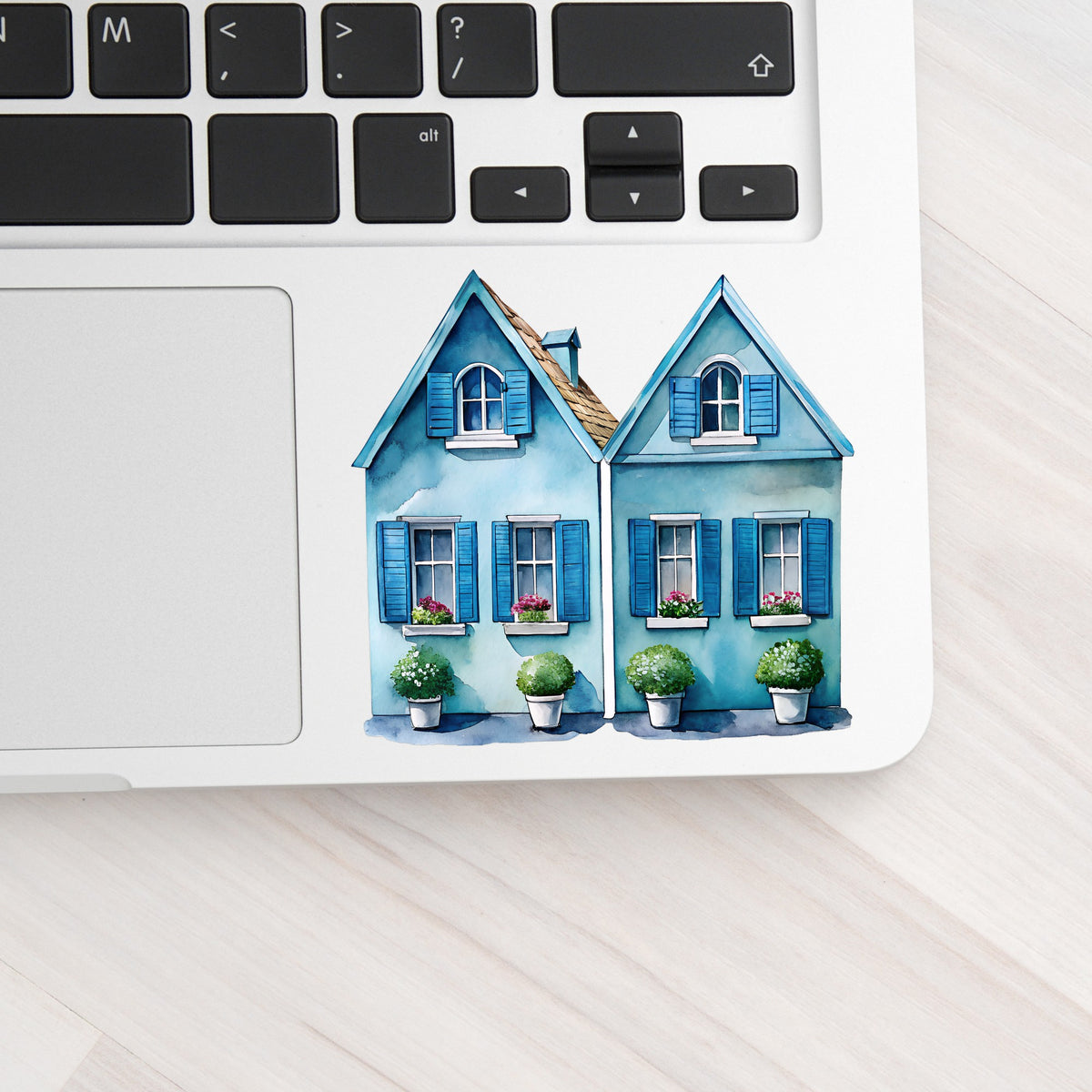 Two Blue Coastal Cottages UV DTF sticker applied to a silver laptop beside the keyboard
