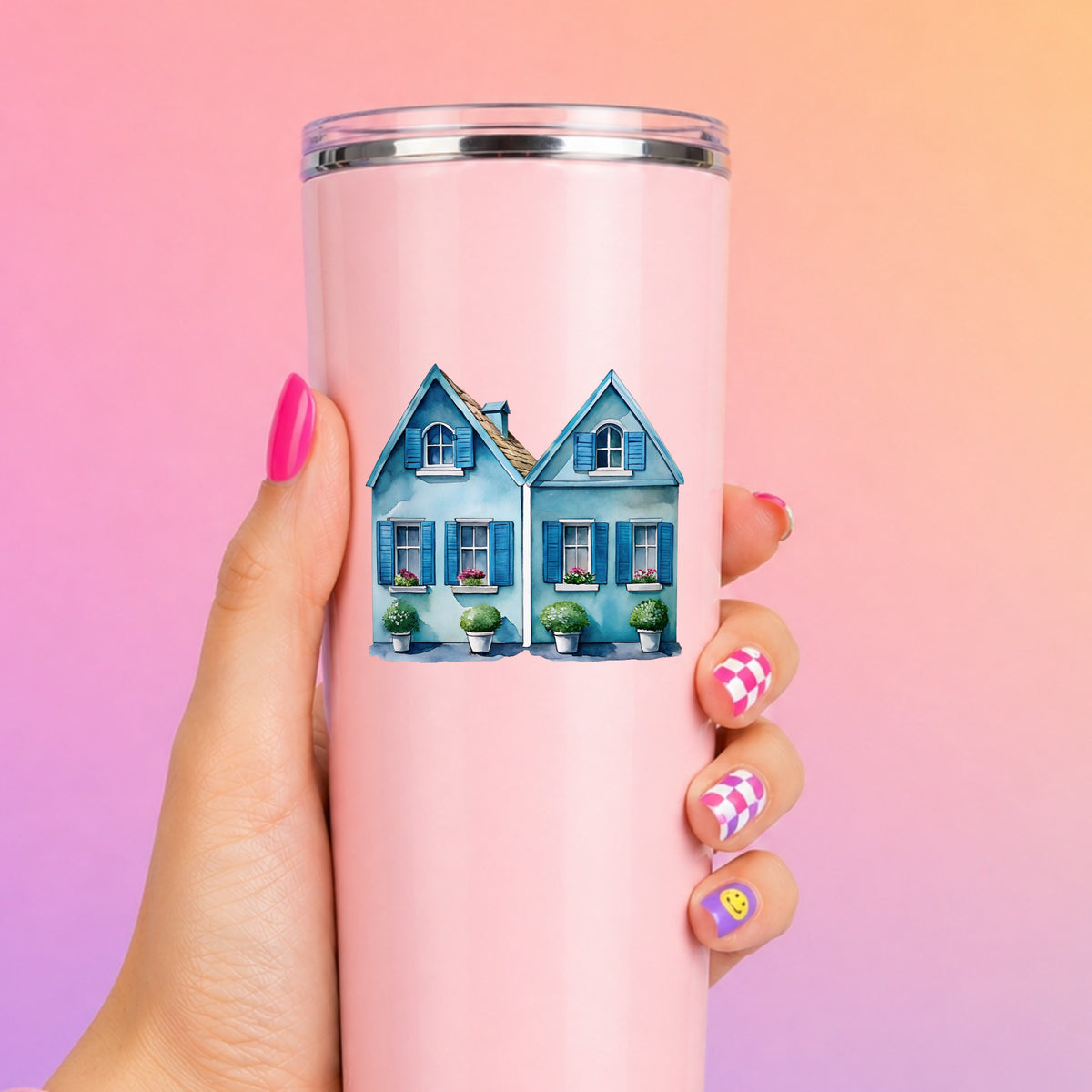 Two Blue Coastal Cottages UV DTF sticker applied to a tall pink tumbler on a pink and orange background