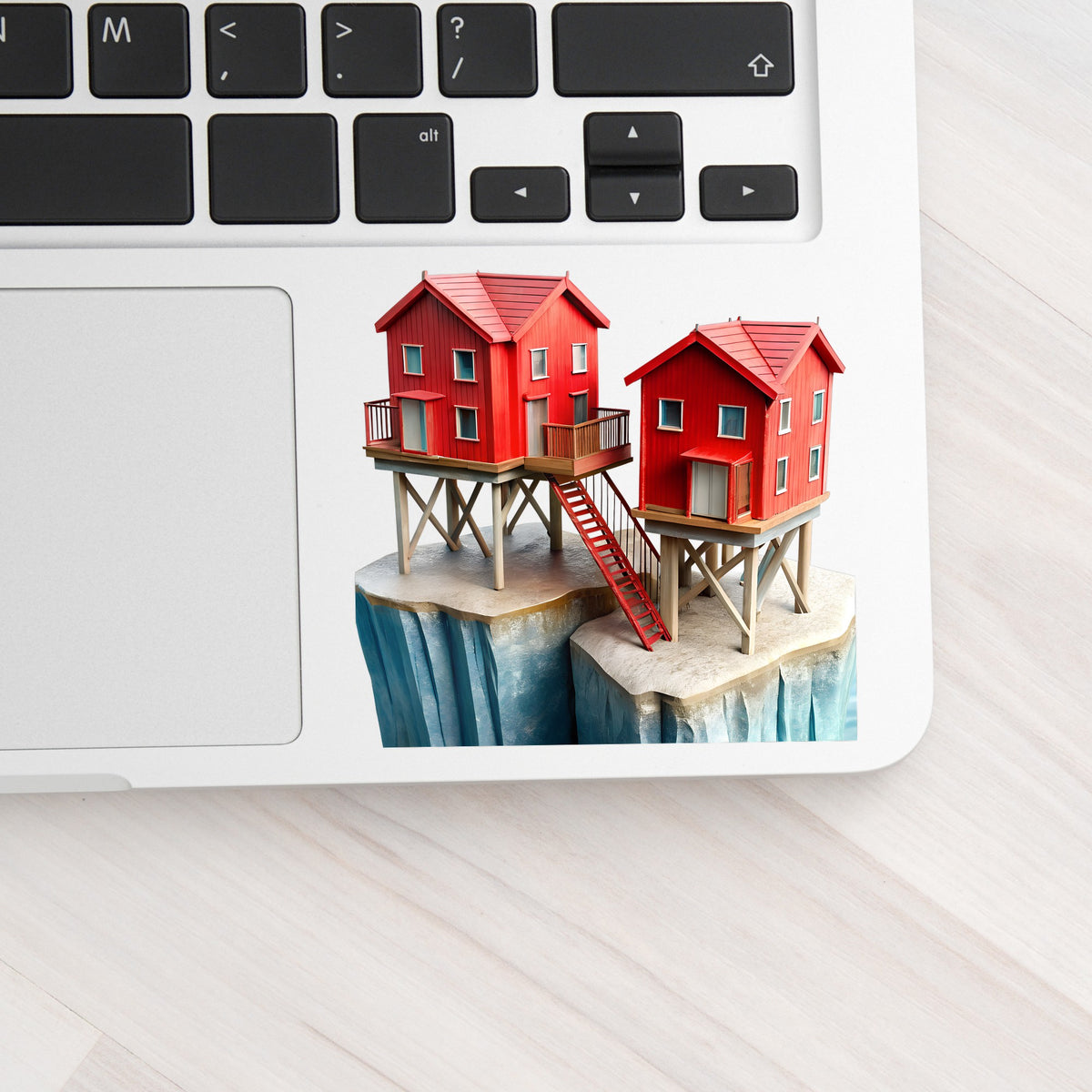 Red Houses On Stilts Cliff UV DTF sticker applied to a silver laptop beside the keyboard