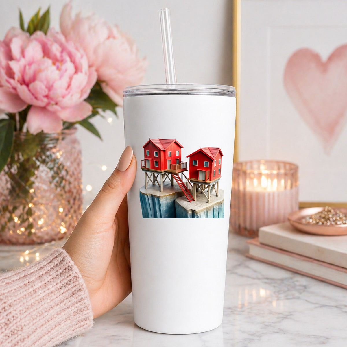 Red Houses On Stilts Cliff UV DTF sticker applied to a white straw tumbler beside pink peonies