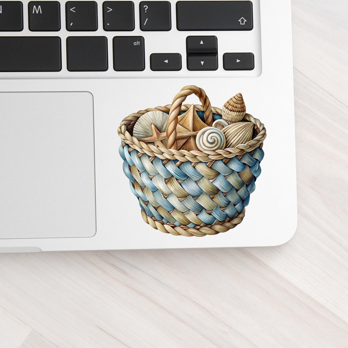Woven Basket Of Seashells UV DTF sticker applied to a silver laptop beside the keyboard