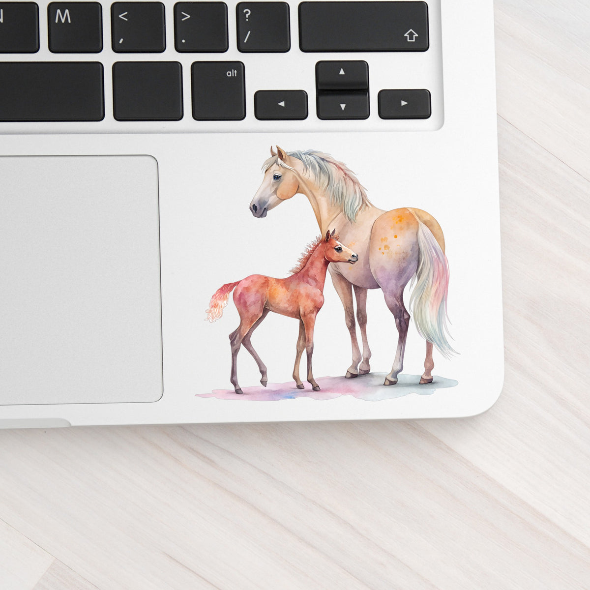 Pastel Mare And Pink Foal UV DTF sticker applied to a silver laptop beside the keyboard