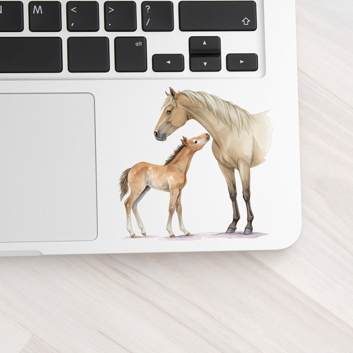 Mare Nuzzling Foal UV DTF sticker applied to a silver laptop beside the keyboard
