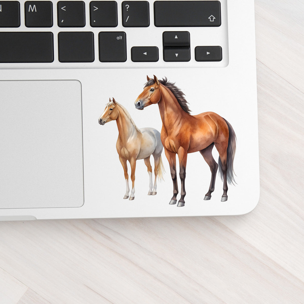 Pair Of Standing Horses Bay And Chestnut UV DTF sticker applied to a silver laptop beside the keyboard