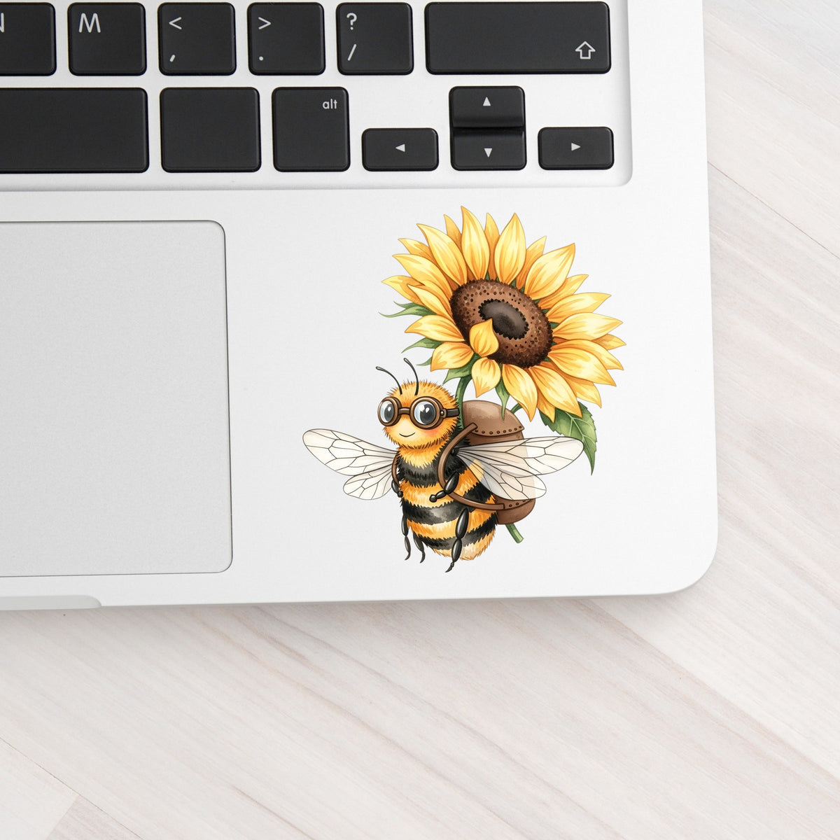 Bee Carrying Sunflower UV DTF sticker applied to a silver laptop beside the keyboard