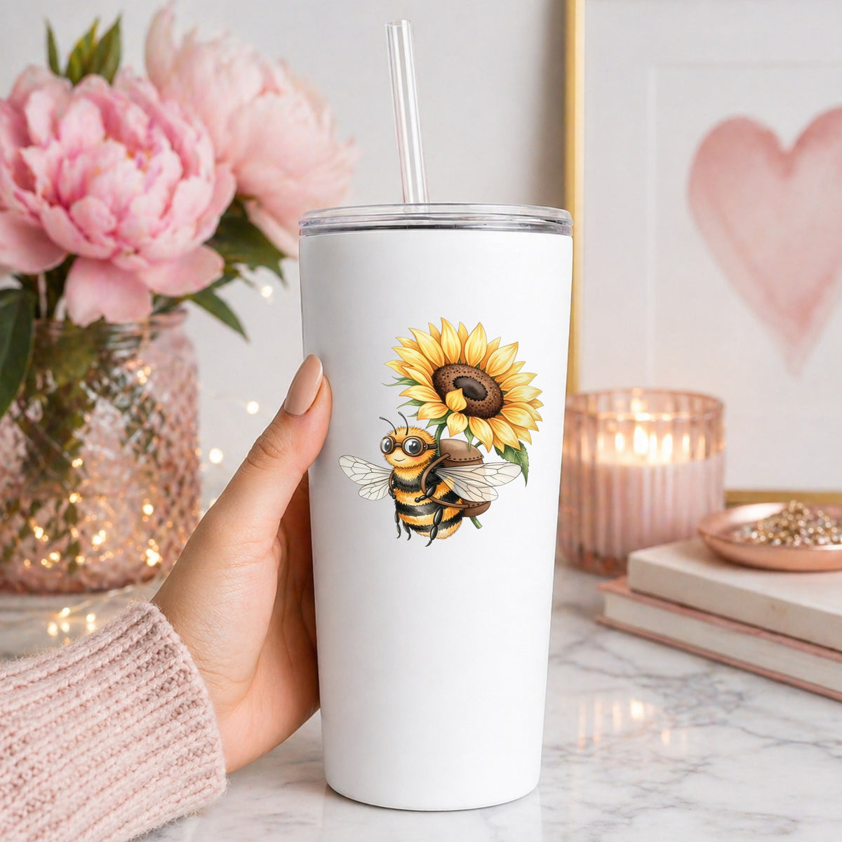 Bee Carrying Sunflower UV DTF sticker applied to a white straw tumbler beside pink peonies
