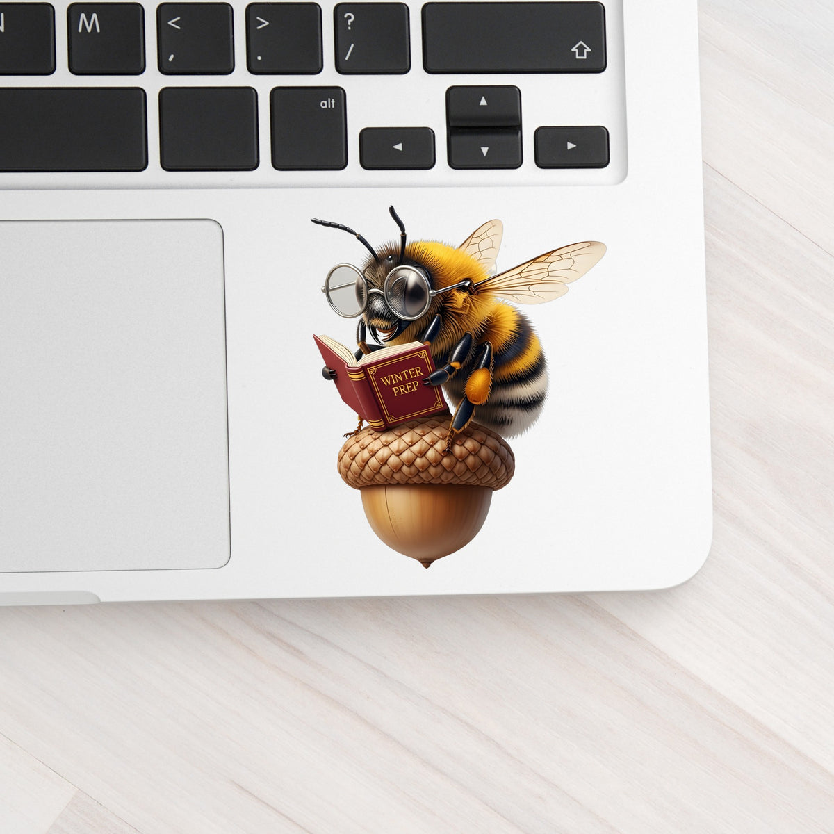 Bee Reading Book On Acorn UV DTF sticker applied to a silver laptop beside the keyboard