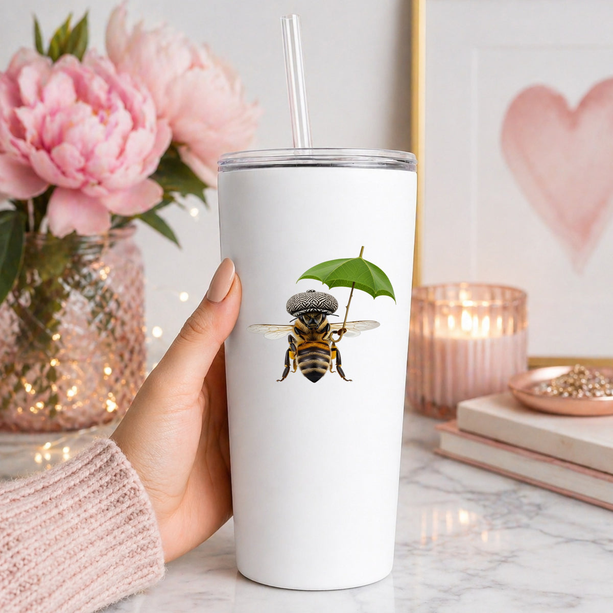 Bee In Flat Cap With Leaf Umbrella UV DTF sticker applied to a white straw tumbler beside pink peonies