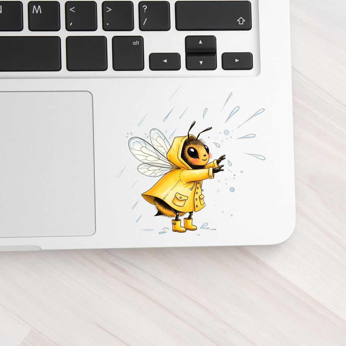 Bee In Yellow Raincoat UV DTF sticker applied to a silver laptop beside the keyboard