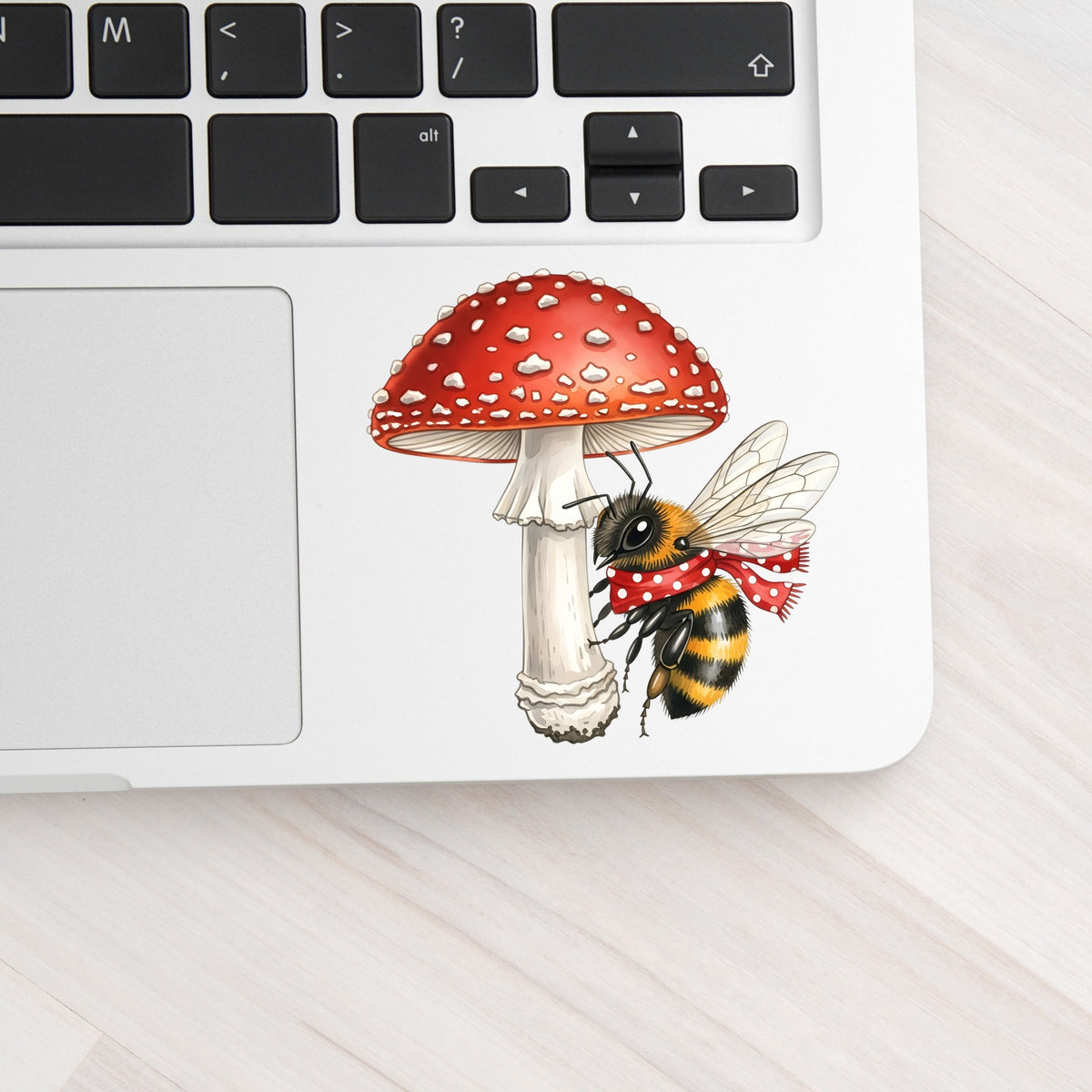 Bee With Red Mushroom UV DTF sticker applied to a silver laptop beside the keyboard
