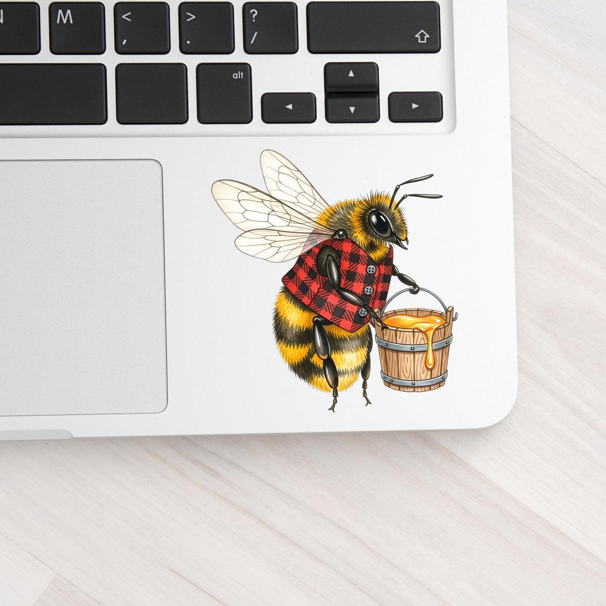 Bee In Plaid Vest With Honey Bucket UV DTF sticker applied to a silver laptop beside the keyboard