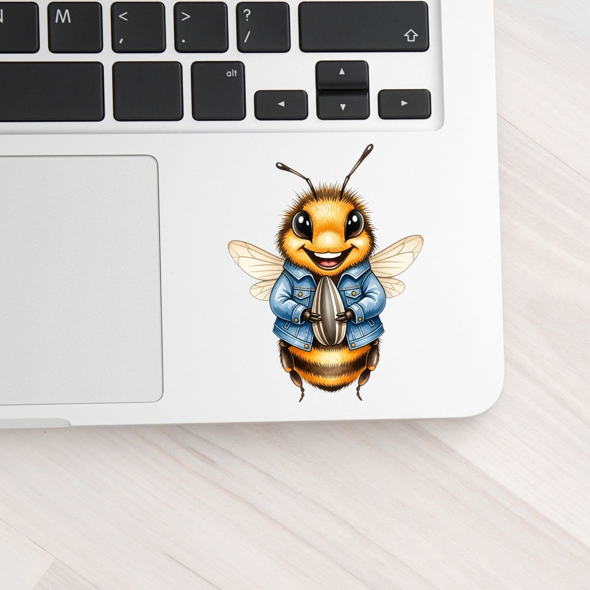 Bee In Denim Jacket With Sunflower Seed UV DTF sticker applied to a silver laptop beside the keyboard