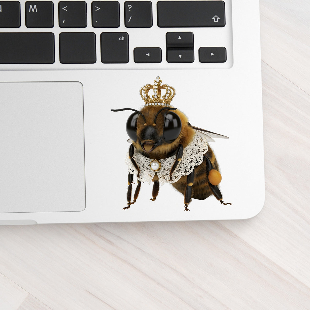 Honeybee With Gold Crown And Lace Collar UV DTF sticker applied to a silver laptop beside the keyboard