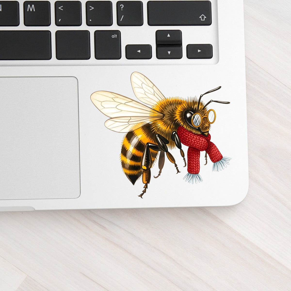 Bee With Spectacles And Red Scarf UV DTF sticker applied to a silver laptop beside the keyboard
