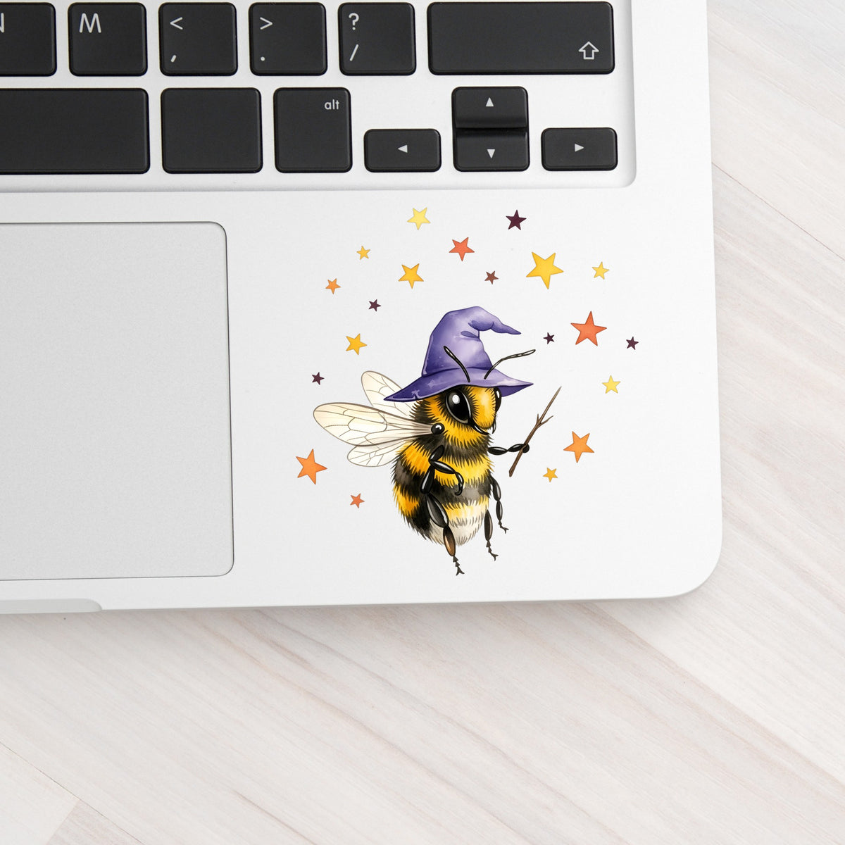 Bee Wizard With Stars UV DTF sticker applied to a silver laptop beside the keyboard