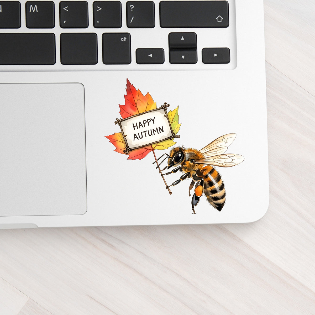 Honeybee Holding Happy Autumn Sign UV DTF sticker applied to a silver laptop beside the keyboard