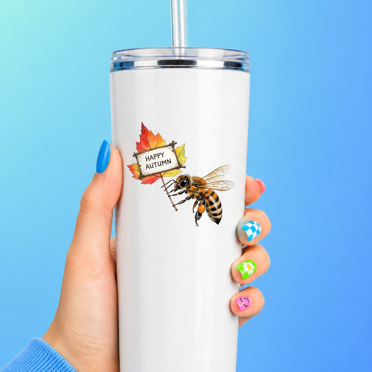 Honeybee Holding Happy Autumn Sign UV DTF sticker applied to a white straw tumbler on a blue background
