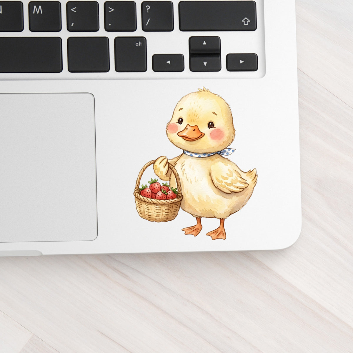 Duckling With Strawberry Basket UV DTF sticker applied to a silver laptop beside the keyboard
