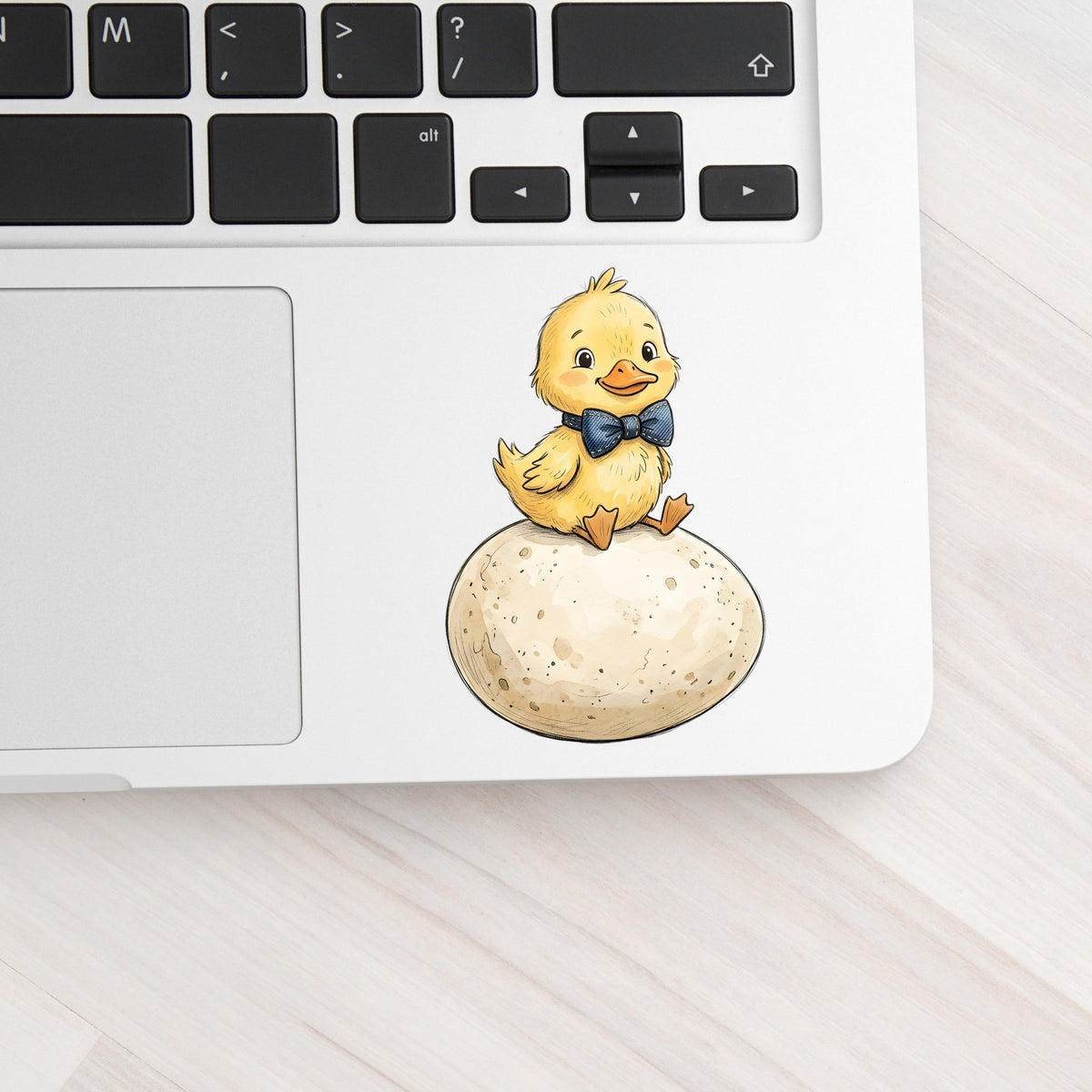 Duckling On Giant Egg UV DTF sticker applied to a silver laptop beside the keyboard
