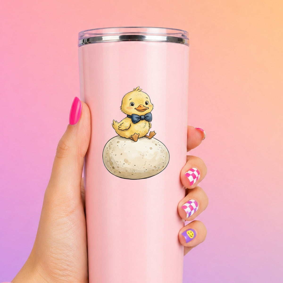 Duckling On Giant Egg UV DTF sticker applied to a tall pink tumbler on a pink and orange background