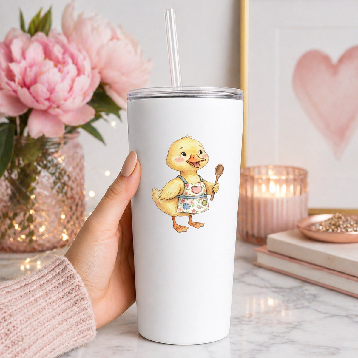 Duckling In Apron With Wooden Spoon UV DTF sticker applied to a white straw tumbler beside pink peonies