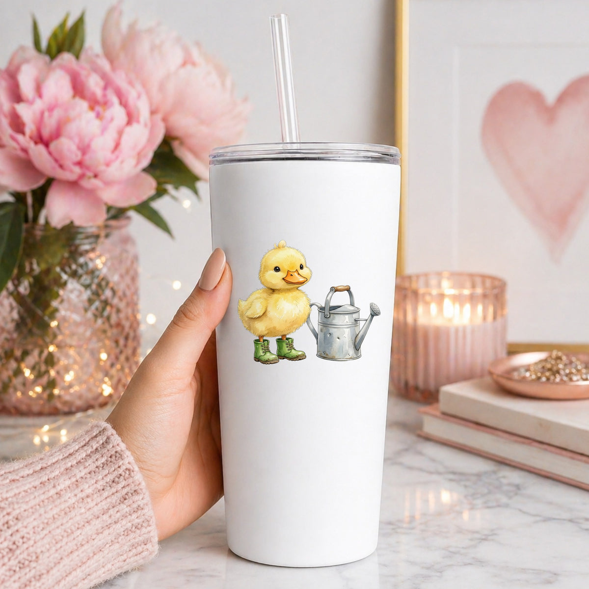 Duckling In Boots With Watering Can UV DTF sticker applied to a white straw tumbler beside pink peonies