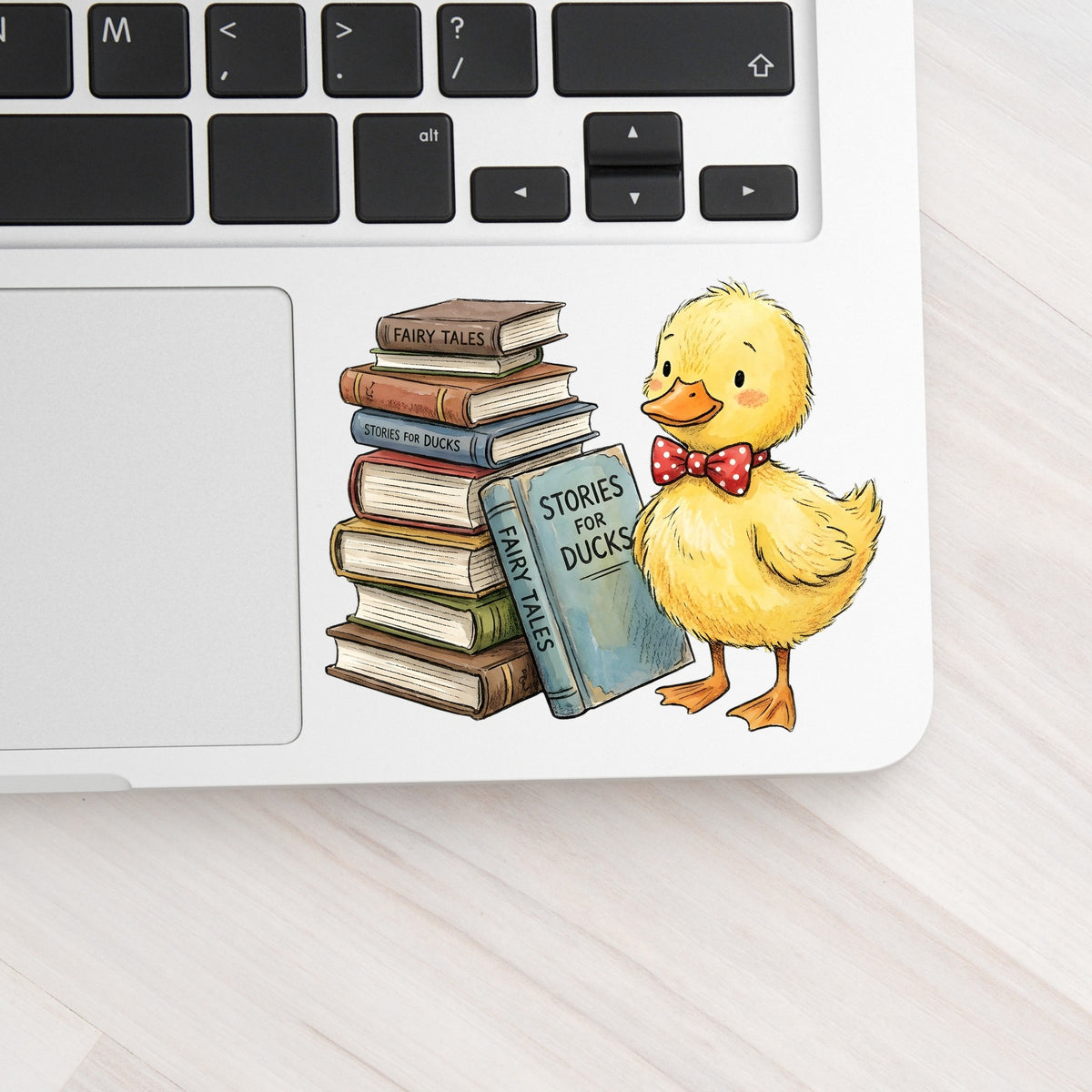 Duckling With Stack Of Storybooks UV DTF sticker applied to a silver laptop beside the keyboard