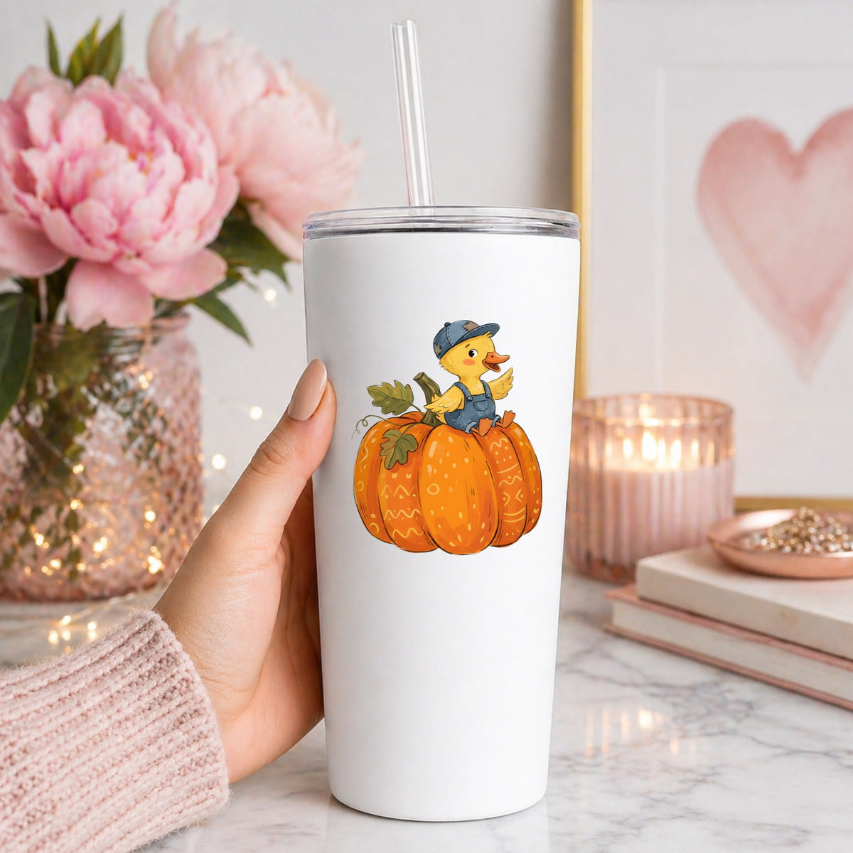 Duckling In Overalls On Pumpkin UV DTF sticker applied to a white straw tumbler beside pink peonies