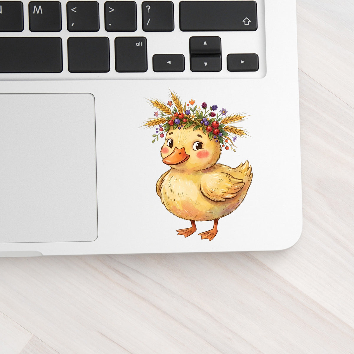 Duckling With Wheat And Berry Crown UV DTF sticker applied to a silver laptop beside the keyboard