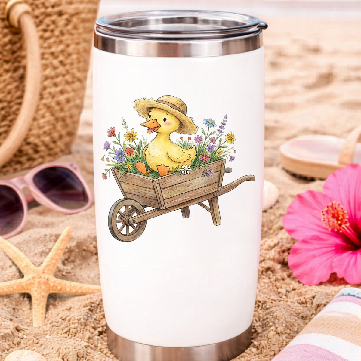 Duckling In Wheelbarrow Of Flowers UV DTF sticker applied to a white travel tumbler on beach sand
